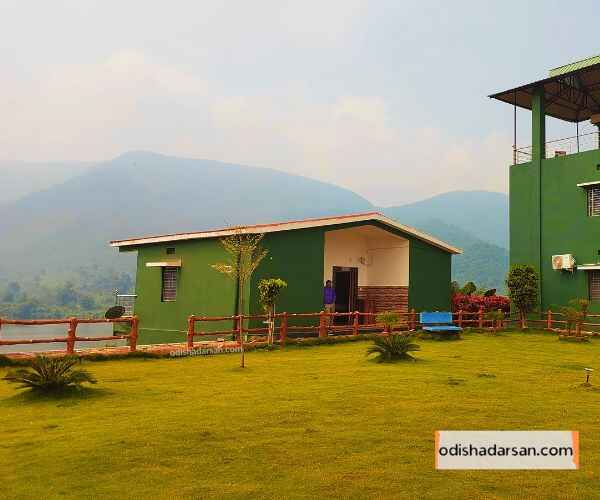 rabandhara-nature-camp-view-showing-park-with-green-grass-a-man-stand-infront-of-the-room-and-mountain-in the-back